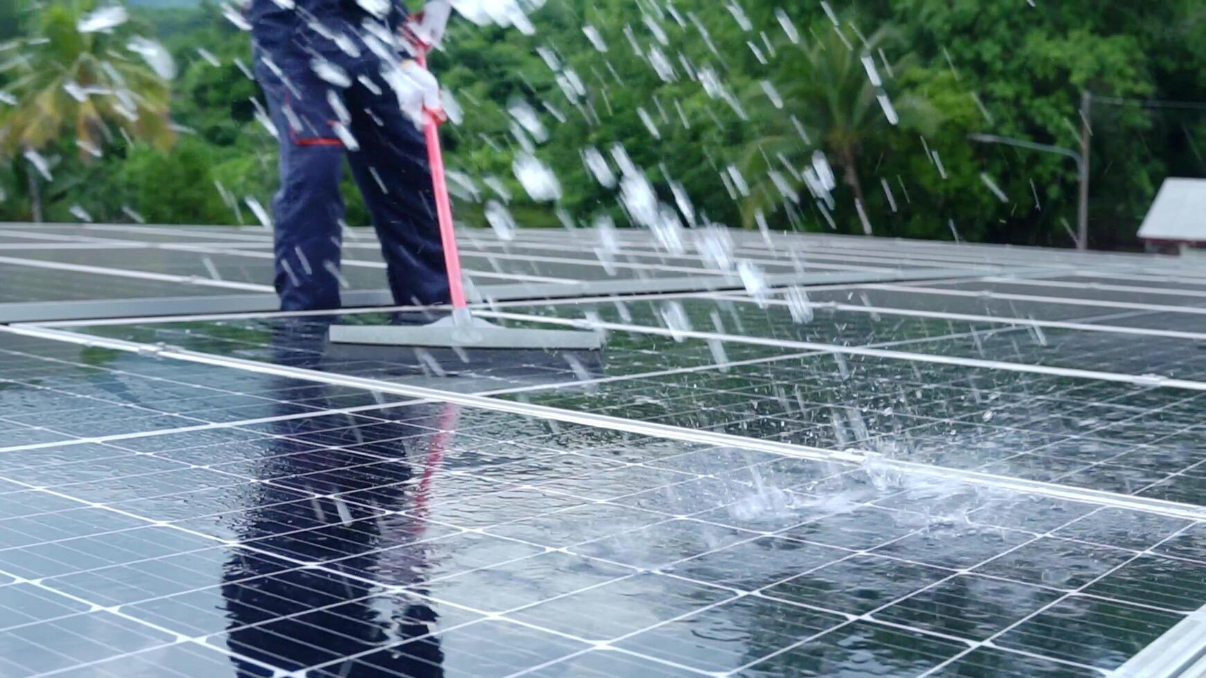 Asian technician Use a mop and water to clean the solar panels dirty with dust to improve the efficiency of solar energy storage. photo