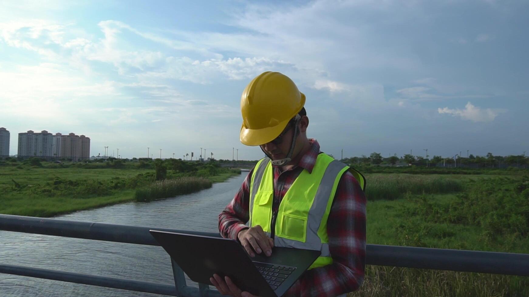 Asian male environmental engineer looking at laptop The scene takes place in a rural area with a river in the background. urban design concept photo
