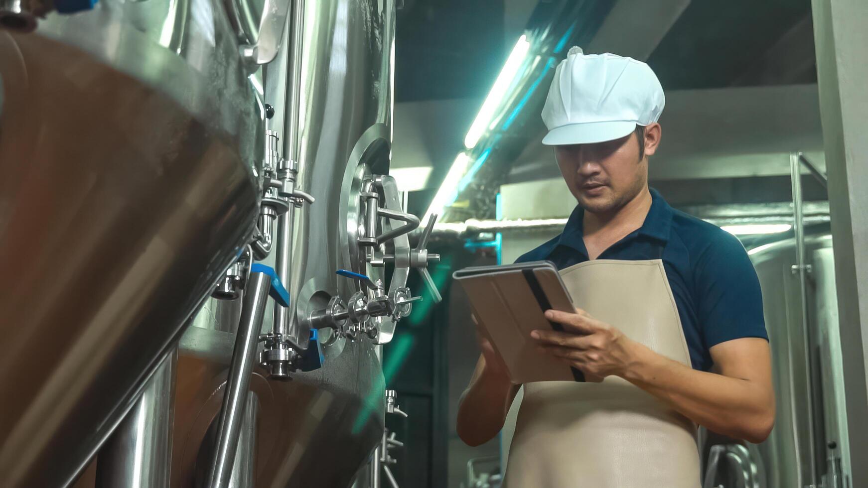 Asian male owner with tablet examining beer quality at craft brewery factory. photo