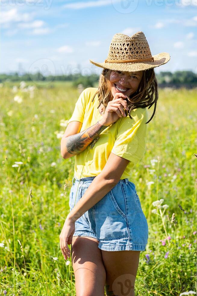 Woman wearing yellow shirt and straw hat standing in sunny field with green grass and wildflowers. photo