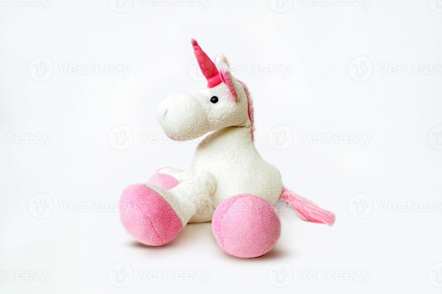 Pink soft unicorn toy sitting at white background. Isolated studio image photo