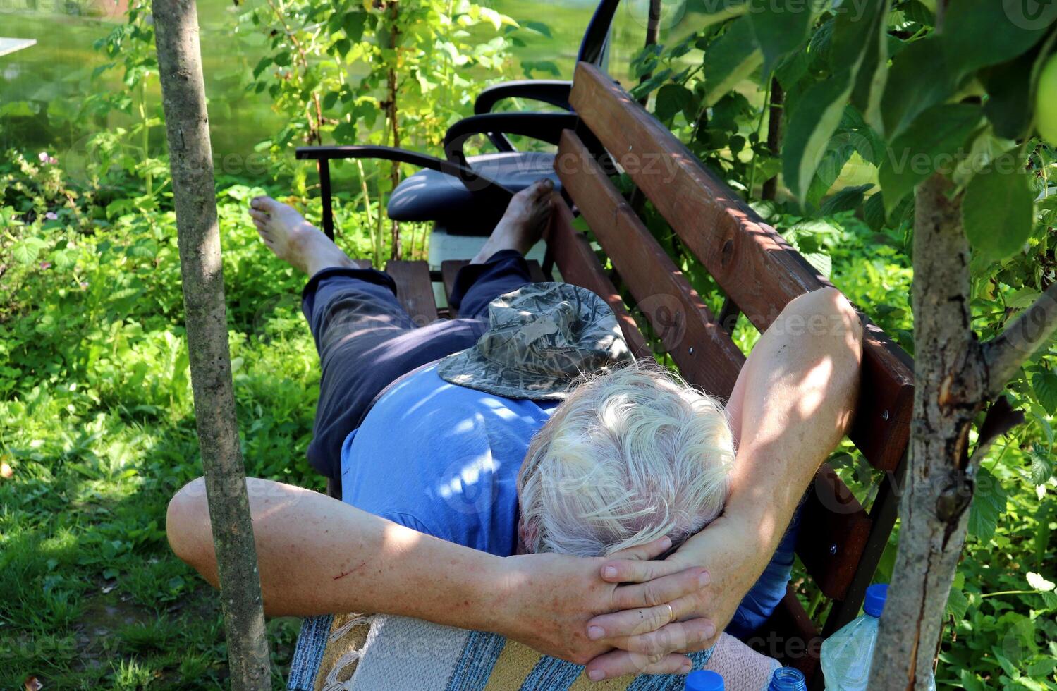 Pensioner man resting after gardening on a bench under a tree photo