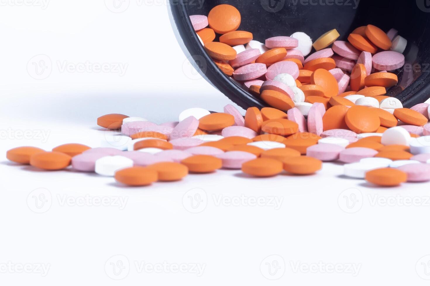Colorful pills spilling out of black plastic container isolated on white background. photo