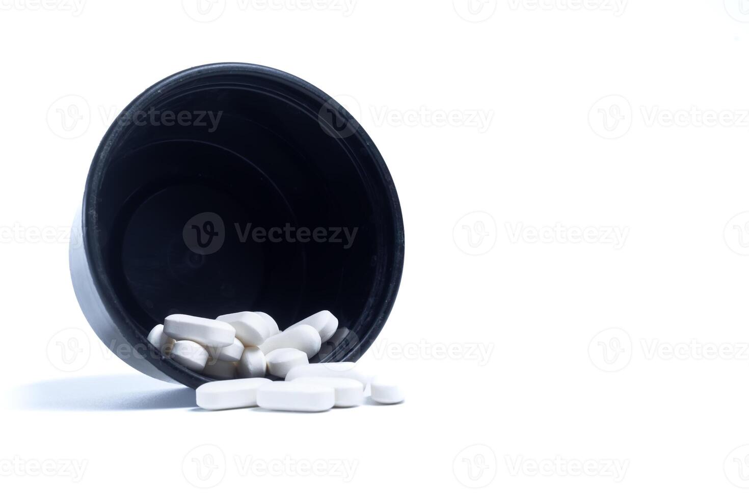 pills spilling out of a black plastic container leaning against a white background. Closeup photo