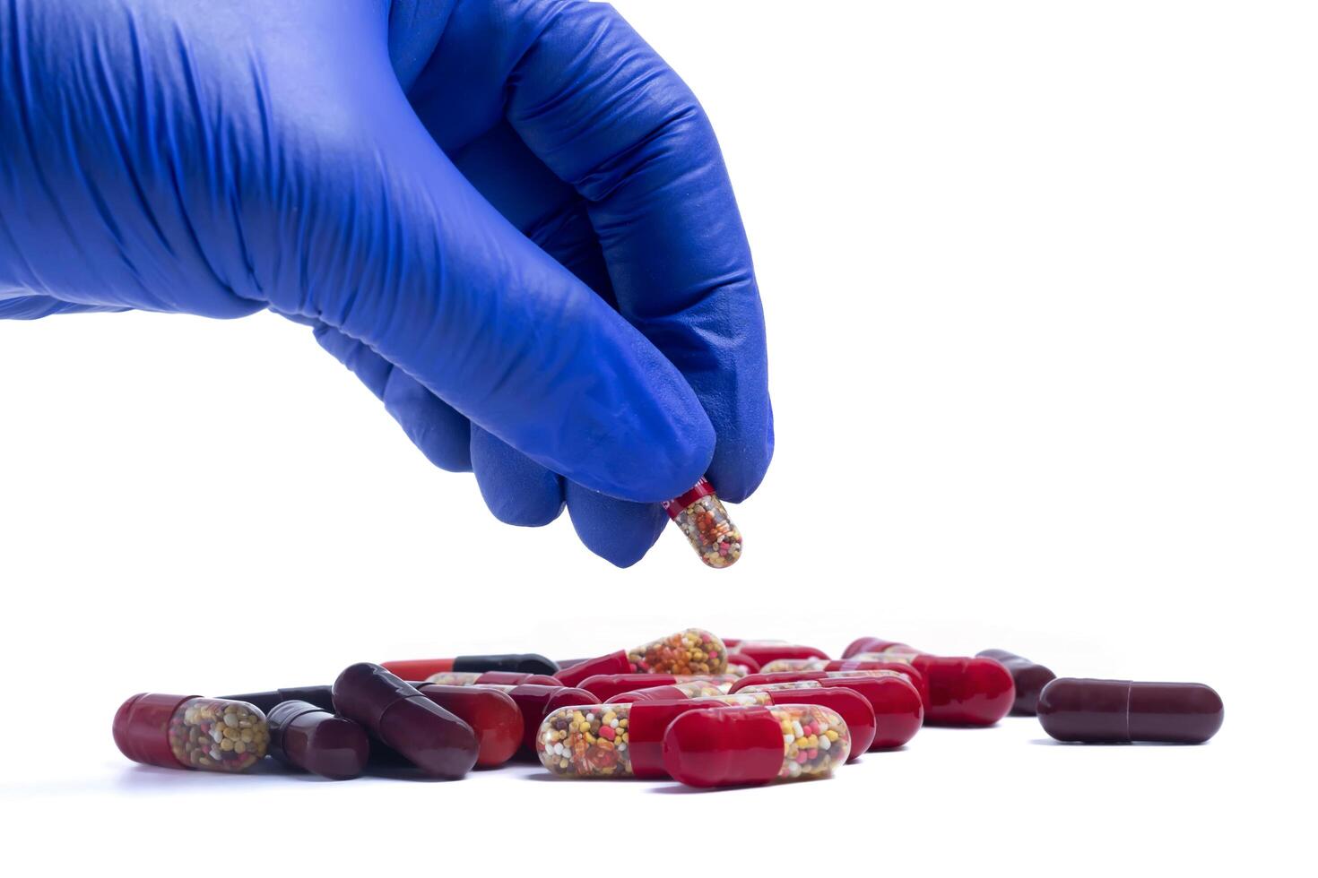 Hand in blue glove picking up a red pill isolated on white background. closeup photo