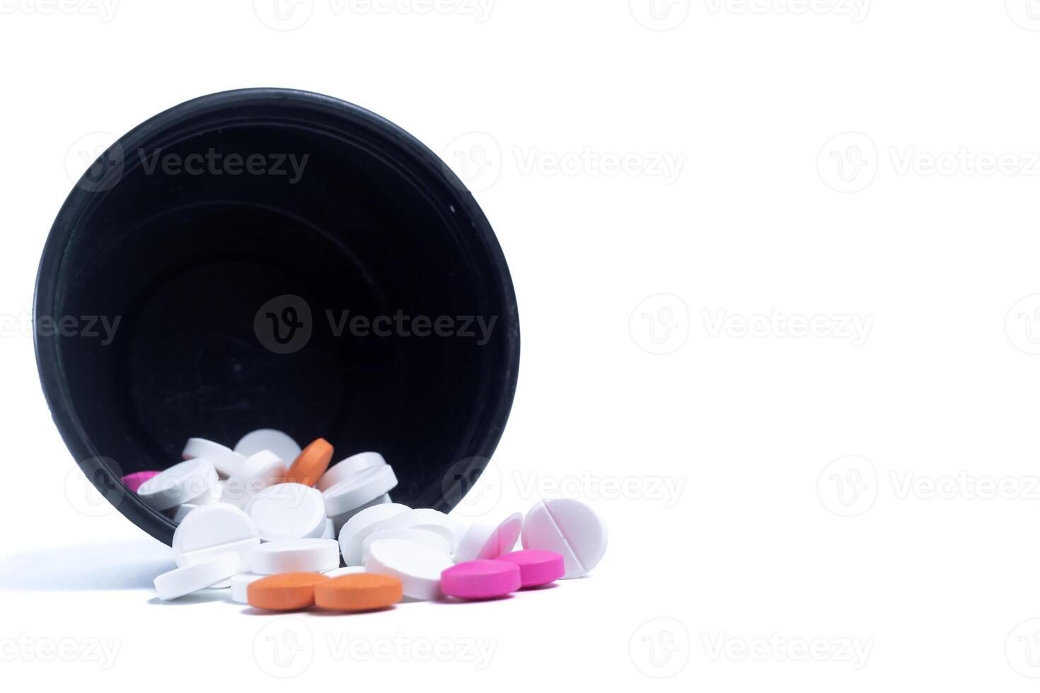 Pills spilling out of a black plastic container leaning against a white background. Medical health care concept. photo