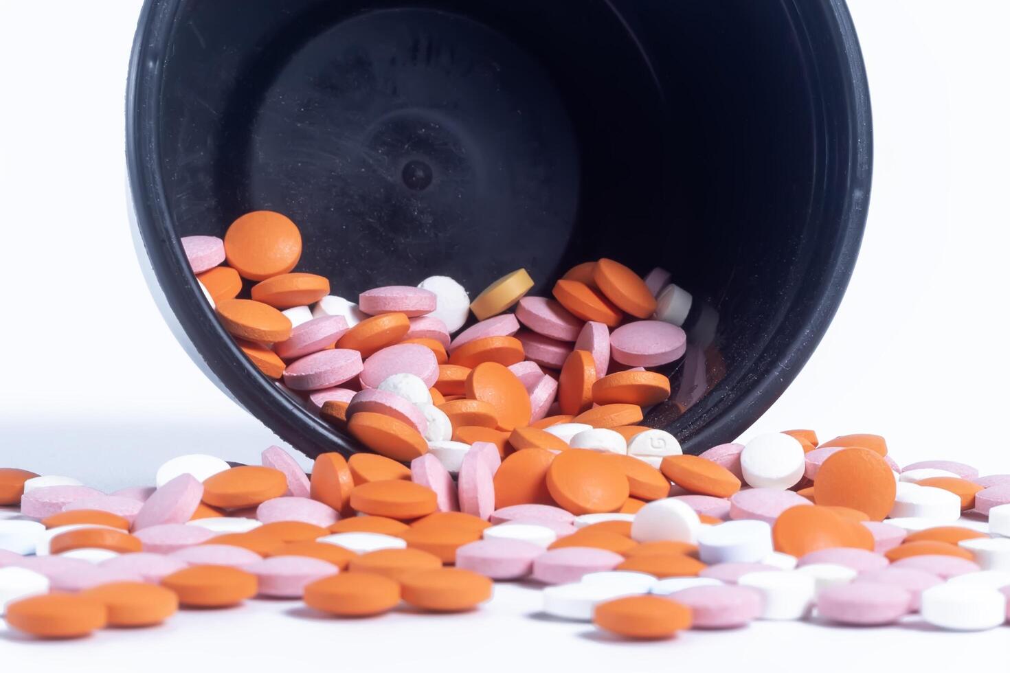 Colorful pills spilling out of black plastic container isolated on white background. photo