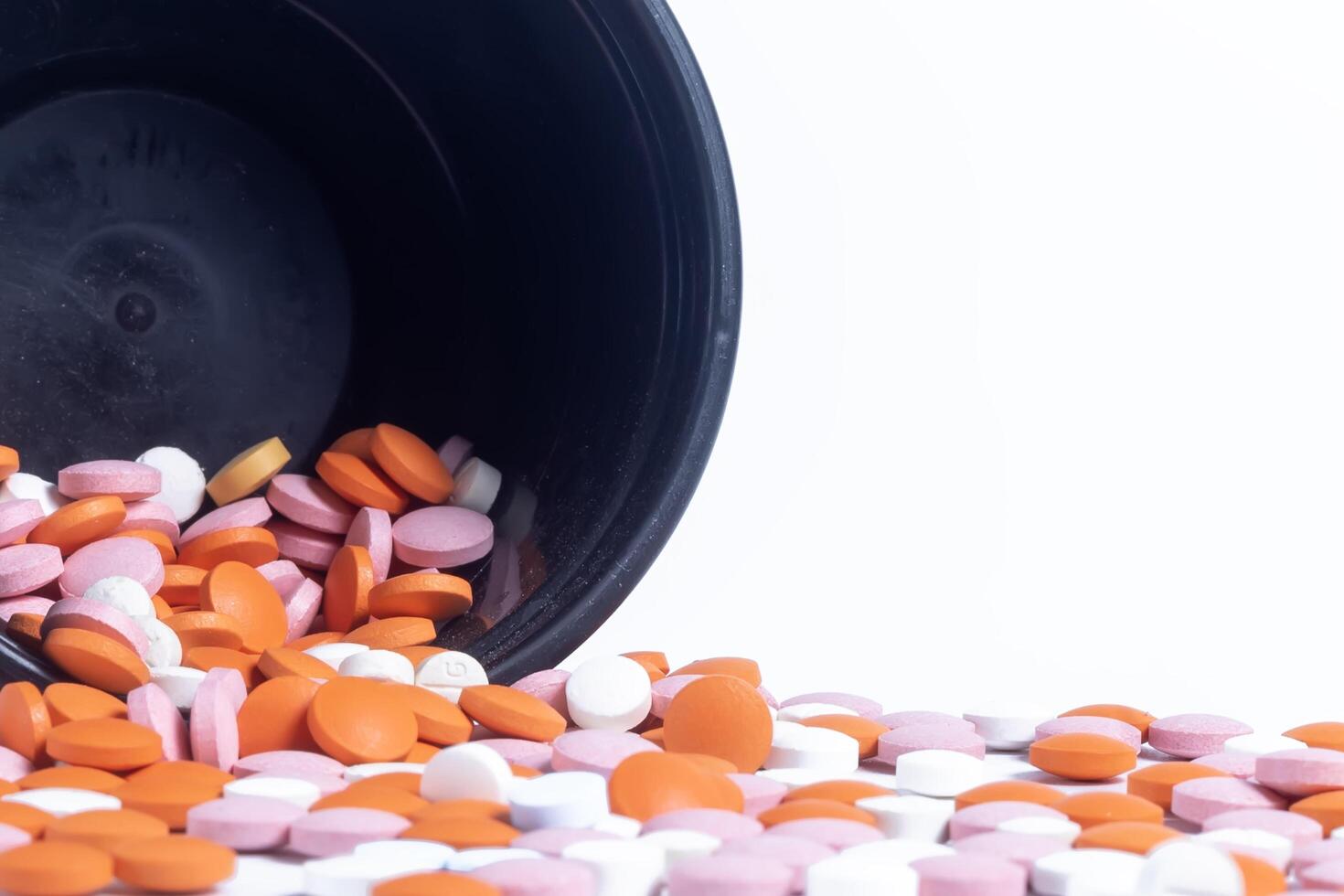 Colorful pills spilling out of black plastic container isolated on white background. photo