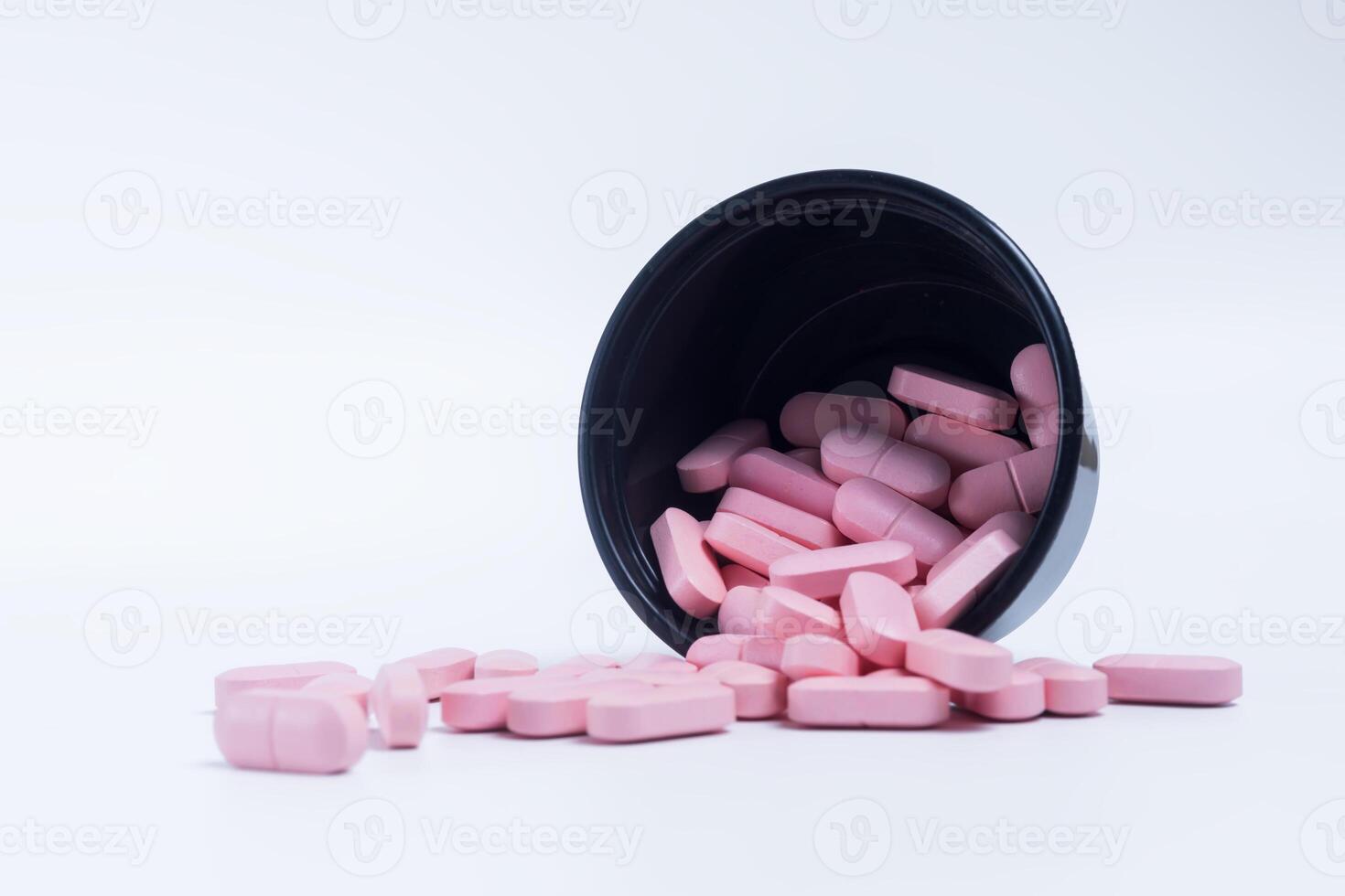 Pink pills spilling out of a black plastic container on a white background. photo