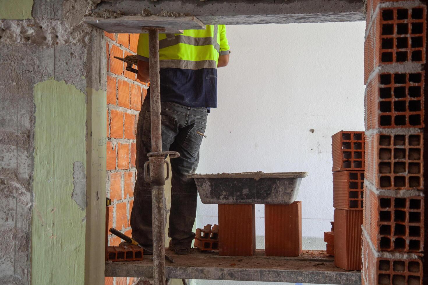 A construction worker applies cement to brick walls during a renovation project, showcasing precision and craftsmanship in a dynamic job site setting. photo