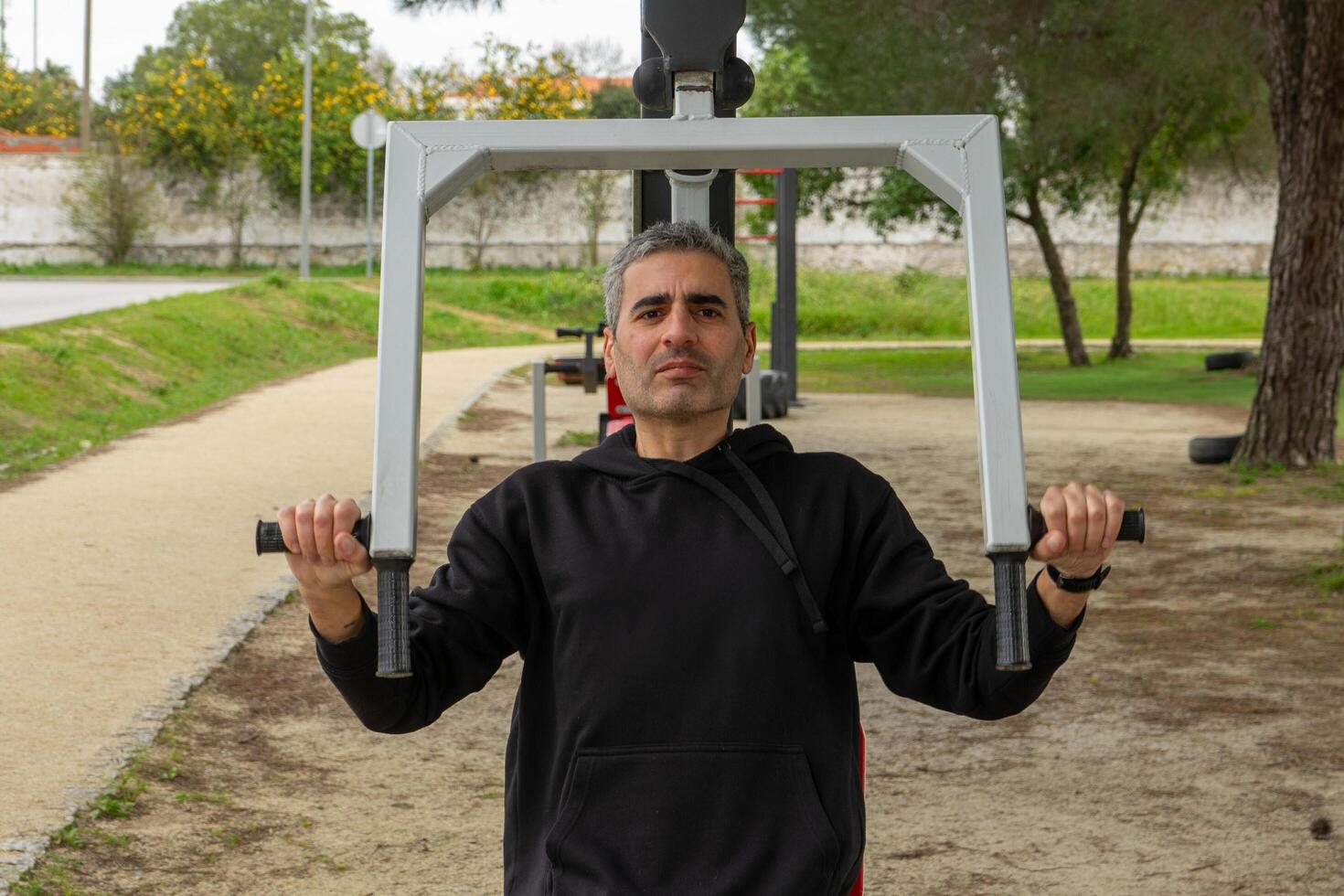 A gray-haired man works out on a chest press machine at an outdoor fitness station in an urban park. He exercises with determination, enjoying the fresh air and staying active. photo