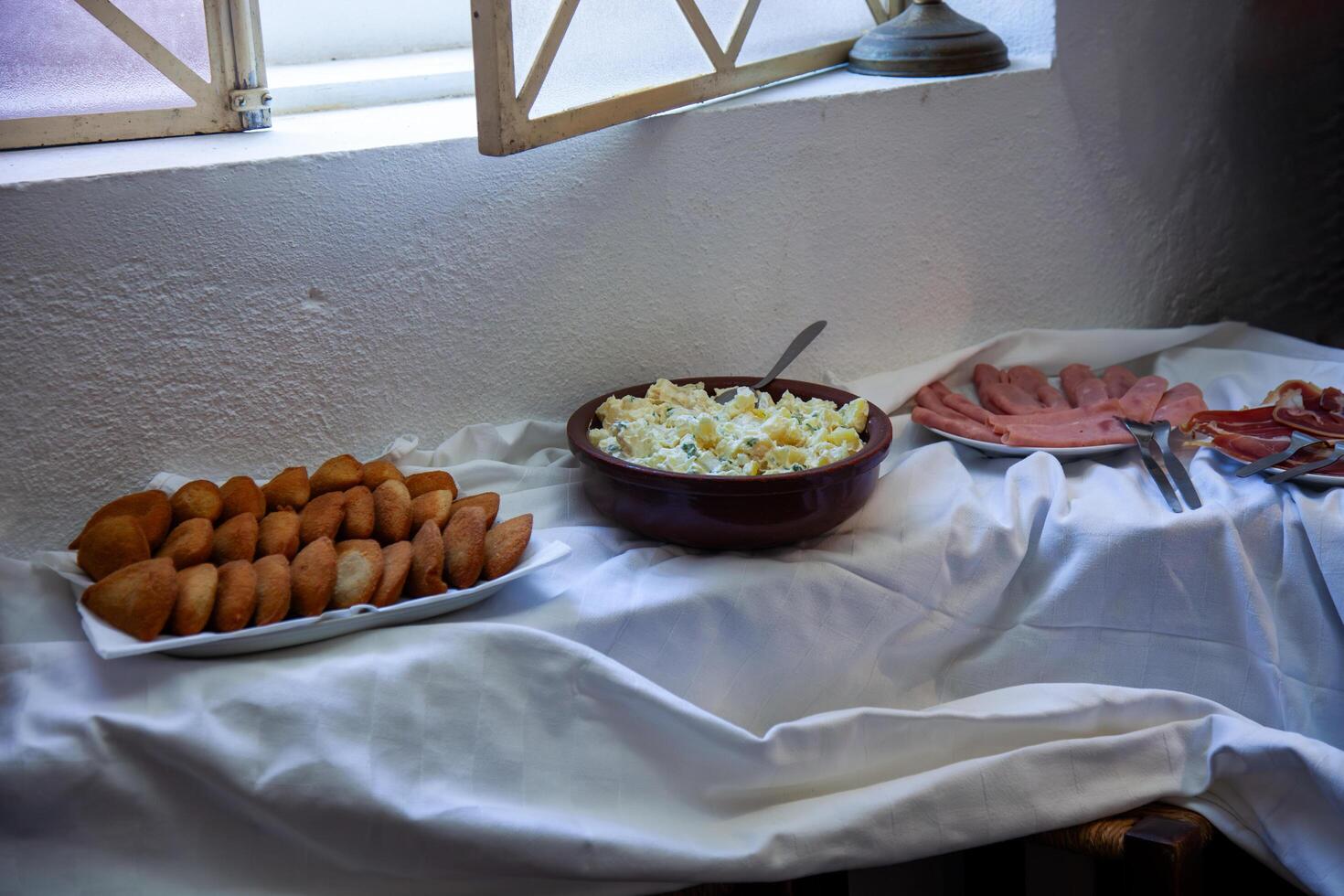 A rustic table set with Russian salad, shrimp rissois, and ham, perfect for a cozy, homestyle meal. Vibrant colors and fresh ingredients make this scene inviting and appetizing. photo