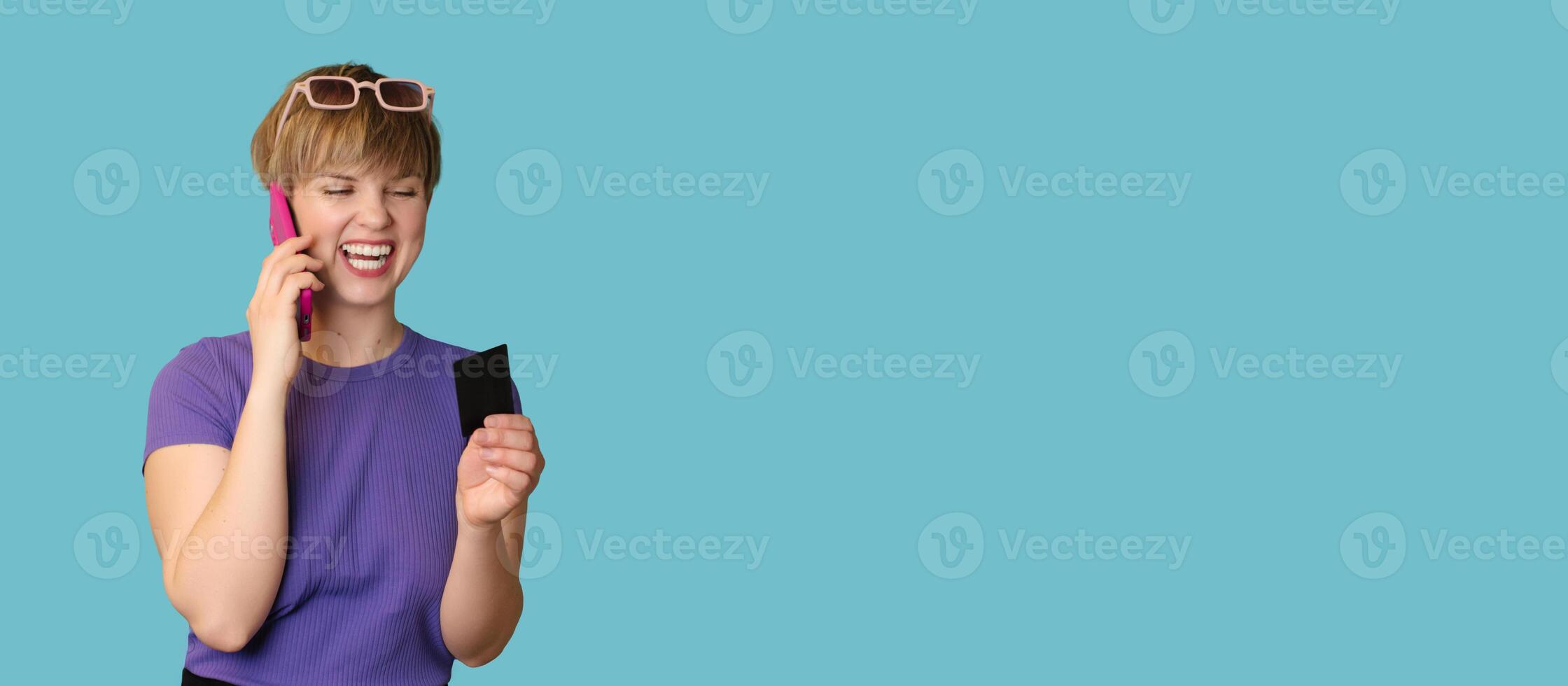 An enthusiastic pretty modern girl advertises mobile banking, online shopping, holds a credit card in her hands and talks on a smartphone. Panoramic image photo