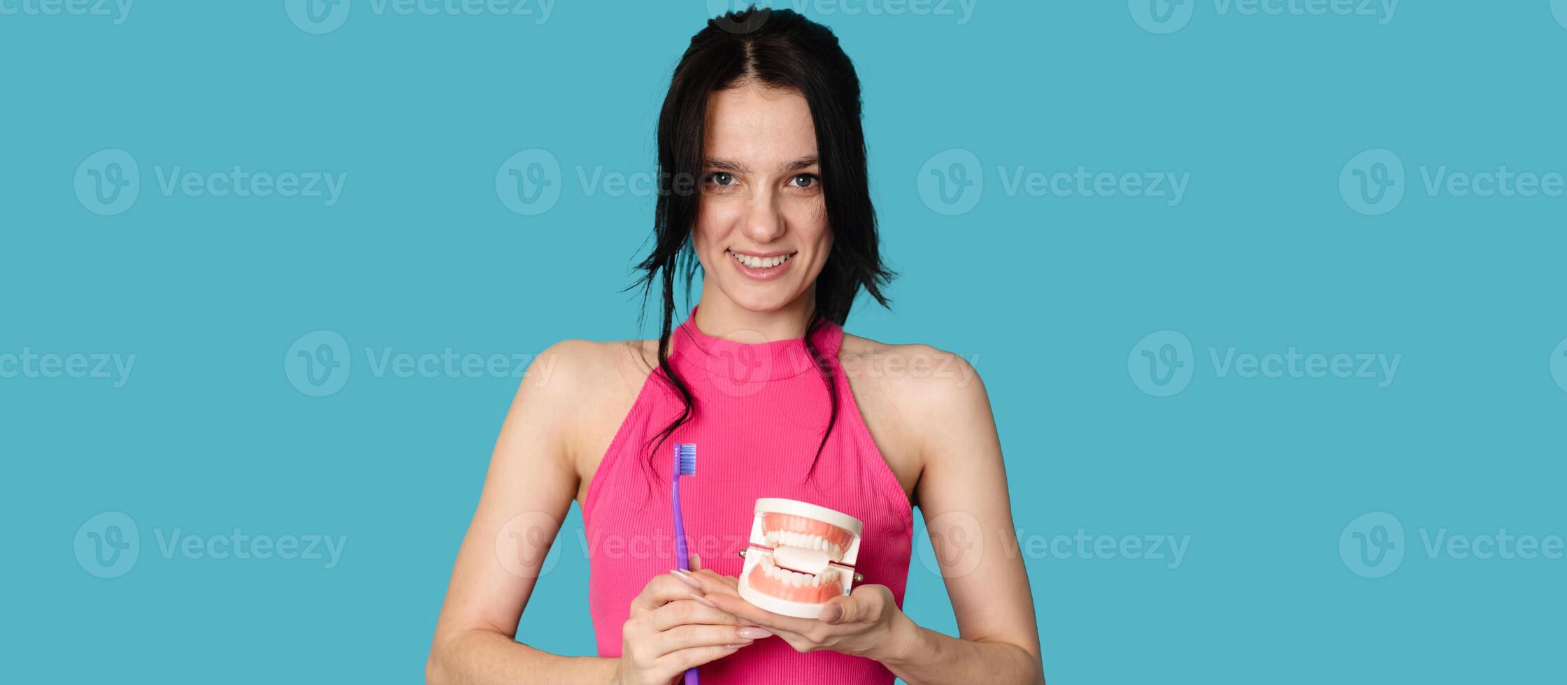 A young Caucasian brunette woman with a toothbrush and a jaw model on a blue background. A panoramic banner with a place for your text. photo
