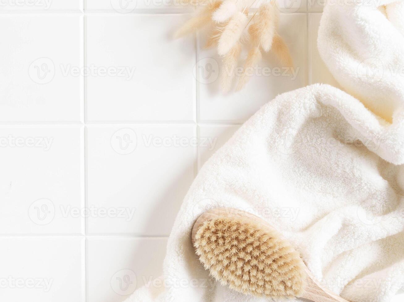 Bath background flat lay with white towels, wood brush and dry flowers on white tiles background photo