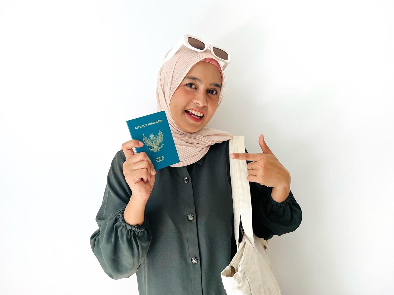 A standing woman with happy face holding Indonesian passport and pointing on her passport isolated on white background. Successful visa application concept photo