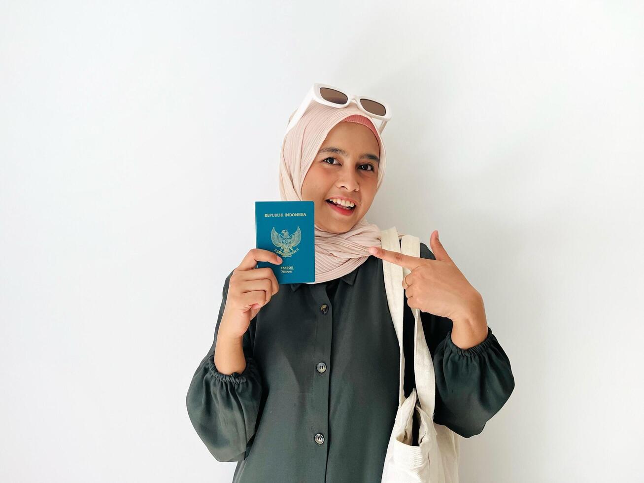 A standing woman with happy face holding Indonesian passport and pointing on her passport isolated on white background. Successful visa application concept photo
