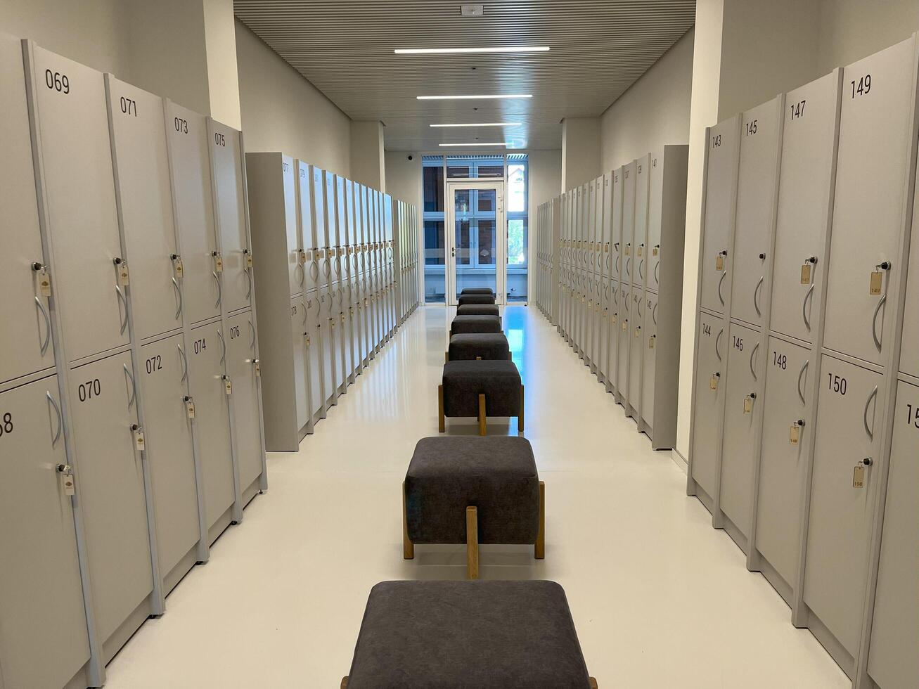 The new lockers, each with a closed steel door, are in two stacked rows and there are chairs lined up in the middle in the new locker room for office staff and visitors. For storage and security photo