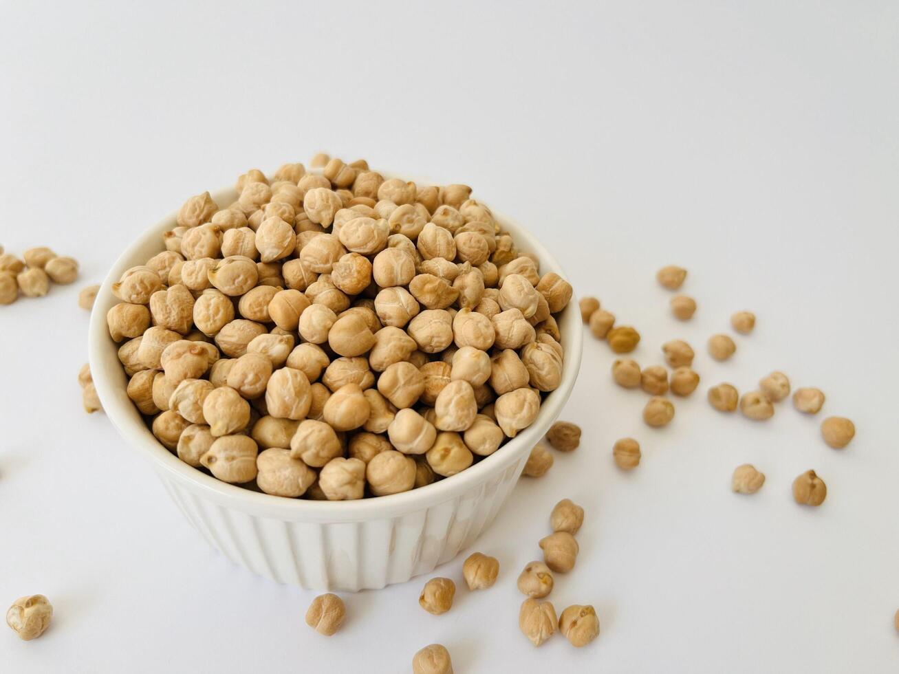 Raw dry chickpea in small ceramic bowl on white background. Traditional ingredient for cooking hummus. Middle Eastern and Mediterranean cuisine. Selected focused photo