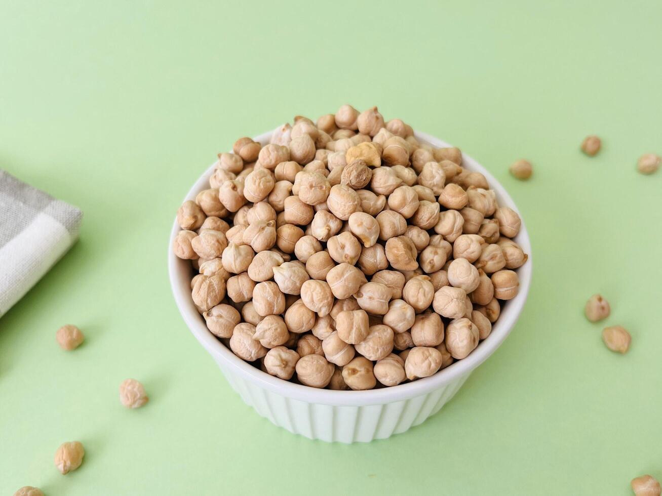Raw dry chickpea in small ceramic bowl on green background. Traditional ingredient for cooking hummus. Middle Eastern and Mediterranean cuisine. Selected focused photo