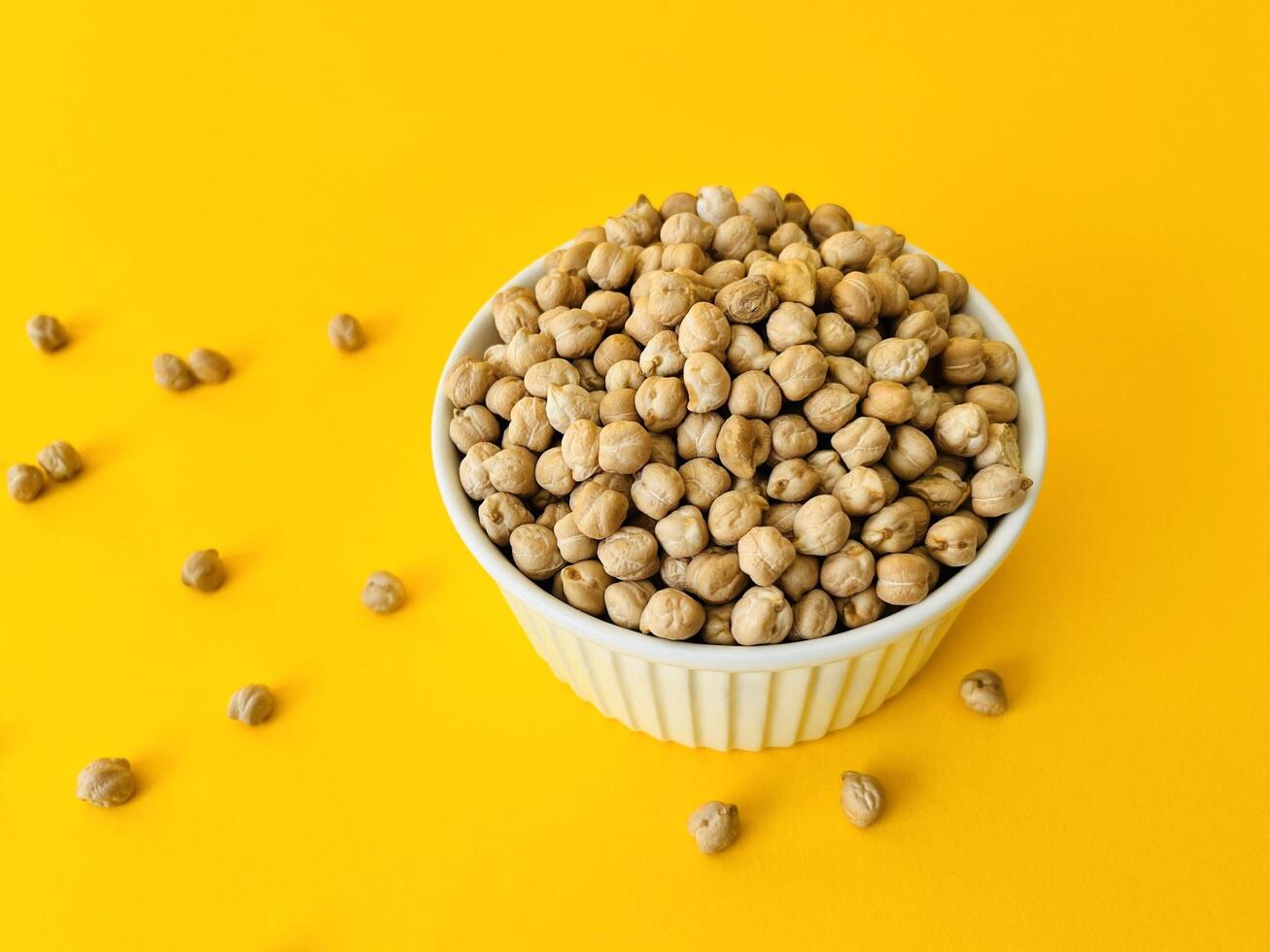 Raw dry chickpea in small ceramic bowl on yellow background. Traditional ingredient for cooking hummus. Middle Eastern and Mediterranean cuisine. Selected focused photo