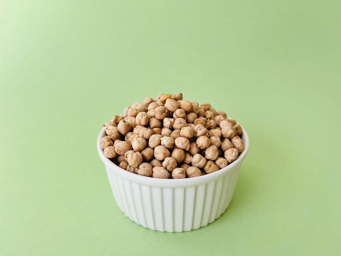Raw dry chickpea in small ceramic bowl on green background. Traditional ingredient for cooking hummus. Middle Eastern and Mediterranean cuisine. Selected focused photo
