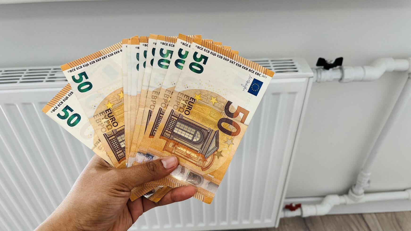 Close-up of a woman hands with banknotes of money in her hands next to a heating radiator. Increase in heating prices in selected households in Europe photo