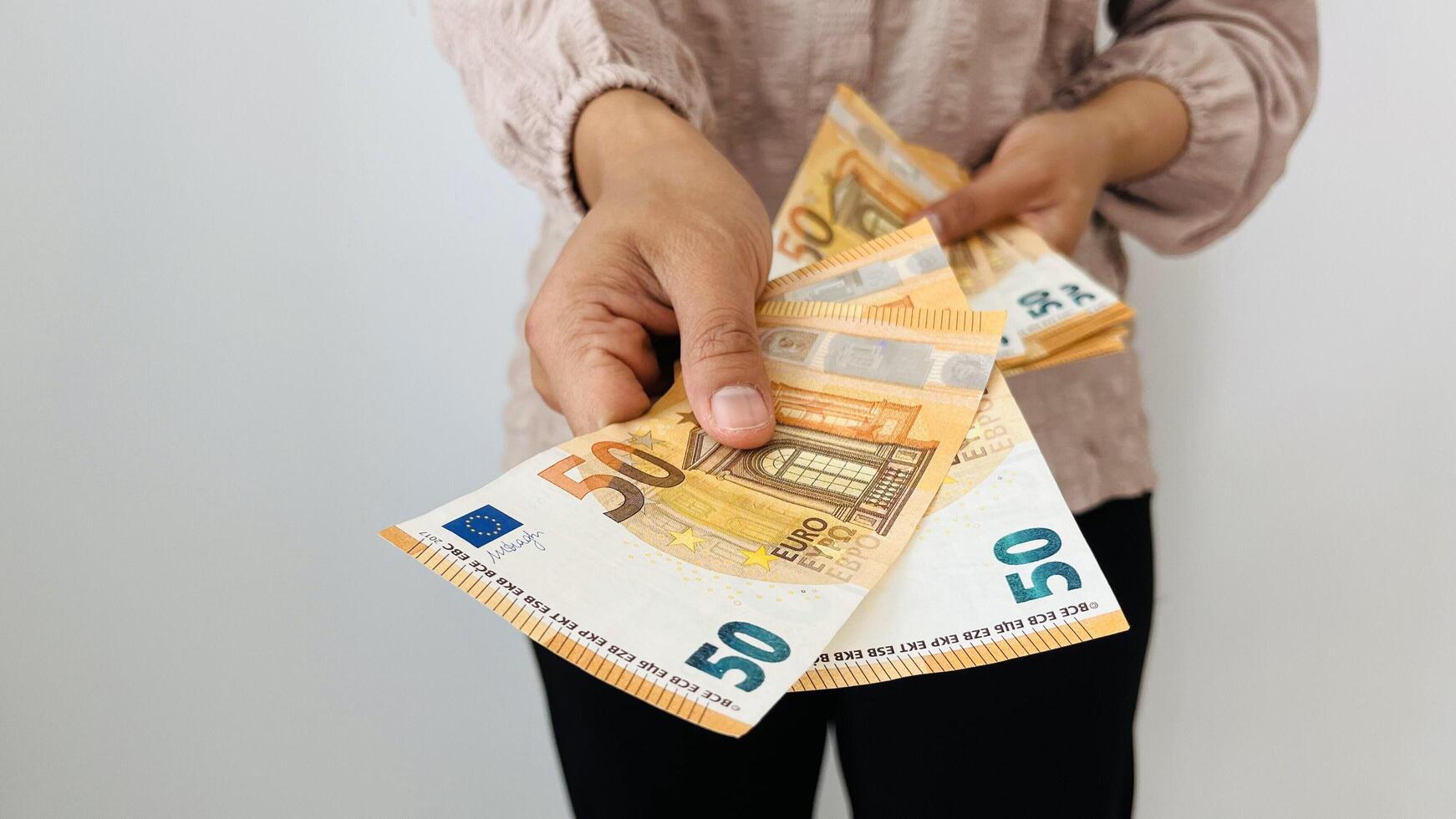 A woman hand offering two 50 euro notes and holding bunch of euro money. Euro banknotes, European Union paper currency. Saving money concept. Finance, business, investment, inflation, purchasing power photo