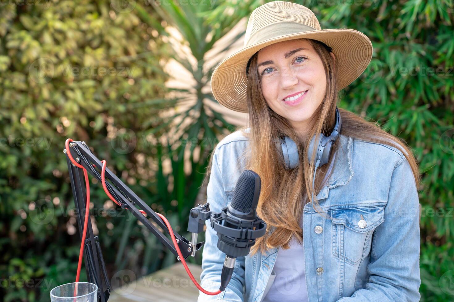 Portrait happy smiling young woman with headphones recording podcast outdoors in spring at sunset. photo