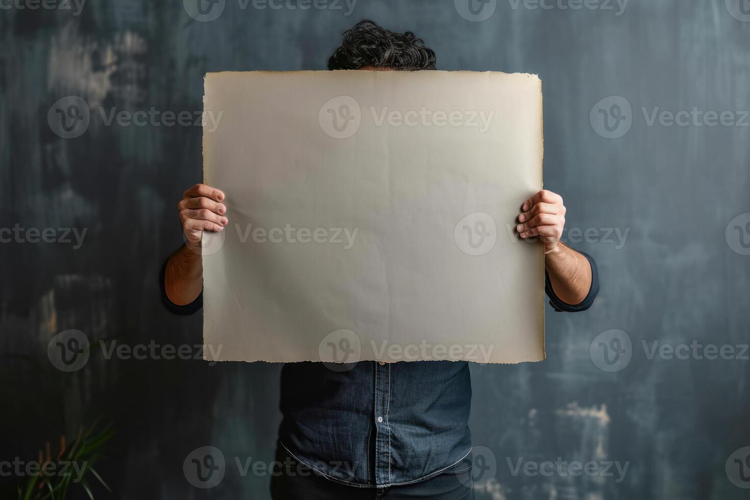 a man holding up an old paper while standing near a plant, photo