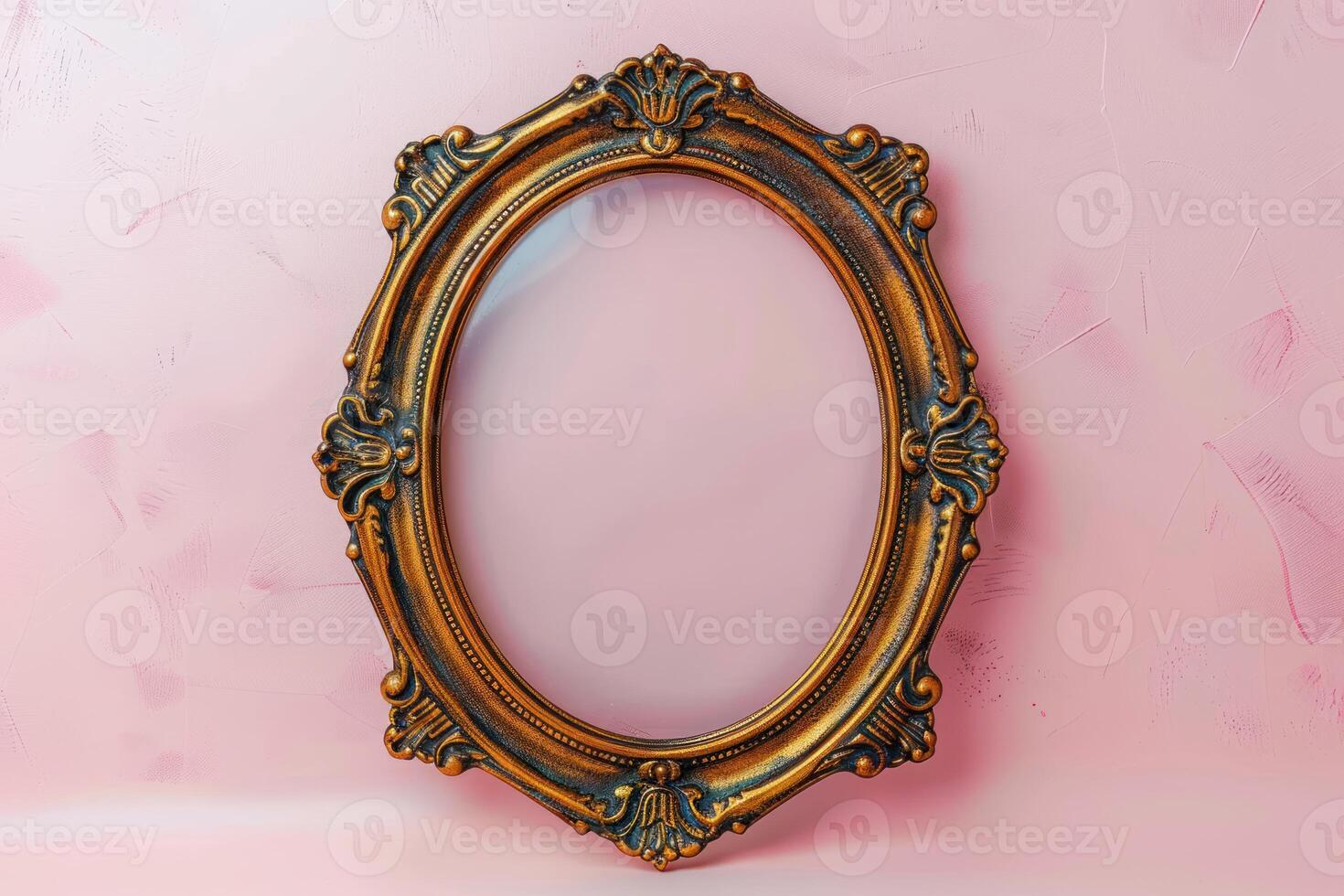 an oval gilded picture frame against a pink wall, photo