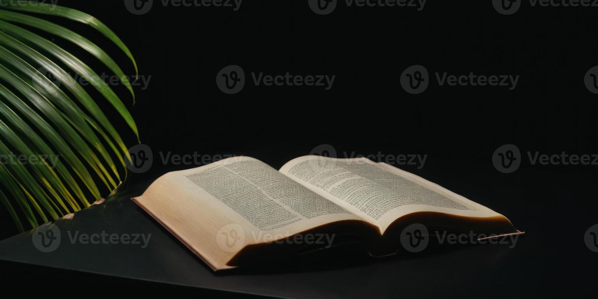 an open book on top of a table next to green leaves, photo