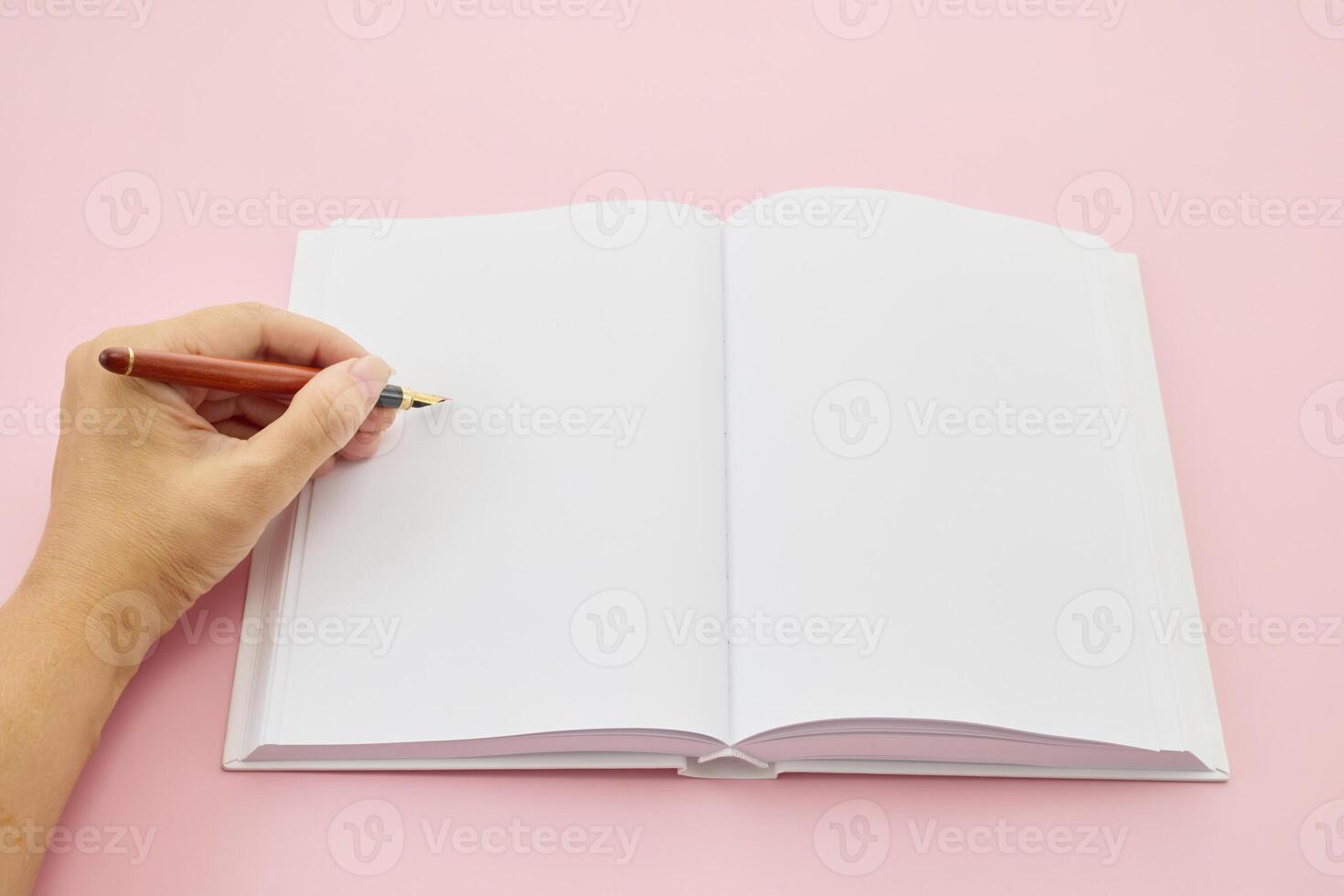 International Left-handers Day. Left hand holding a pen, writing in an open blank journal on a light pink background. photo