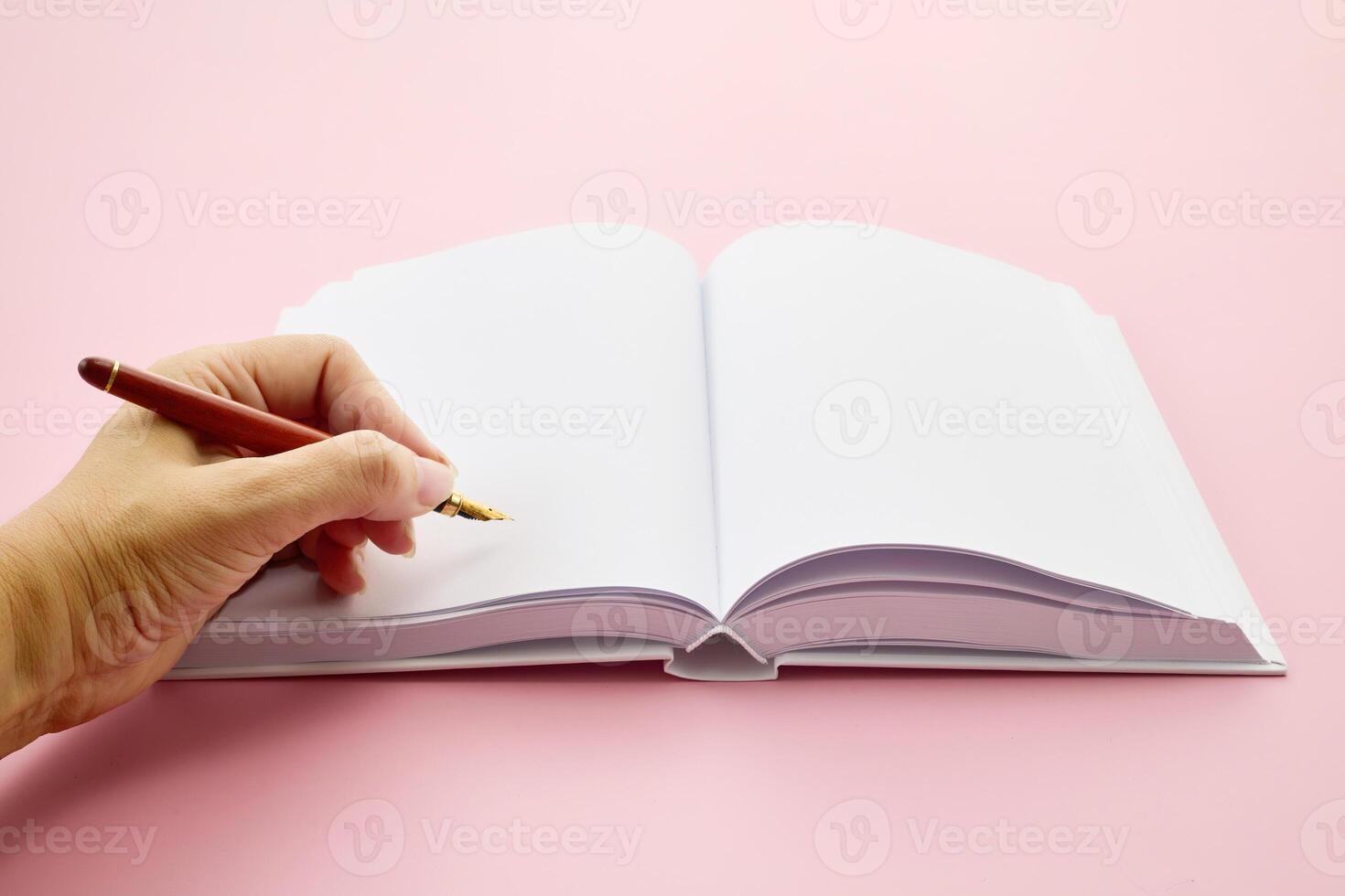 International Left-handers Day. Left Hand holding a pen, writing in an open blank journal on a light pink background. photo