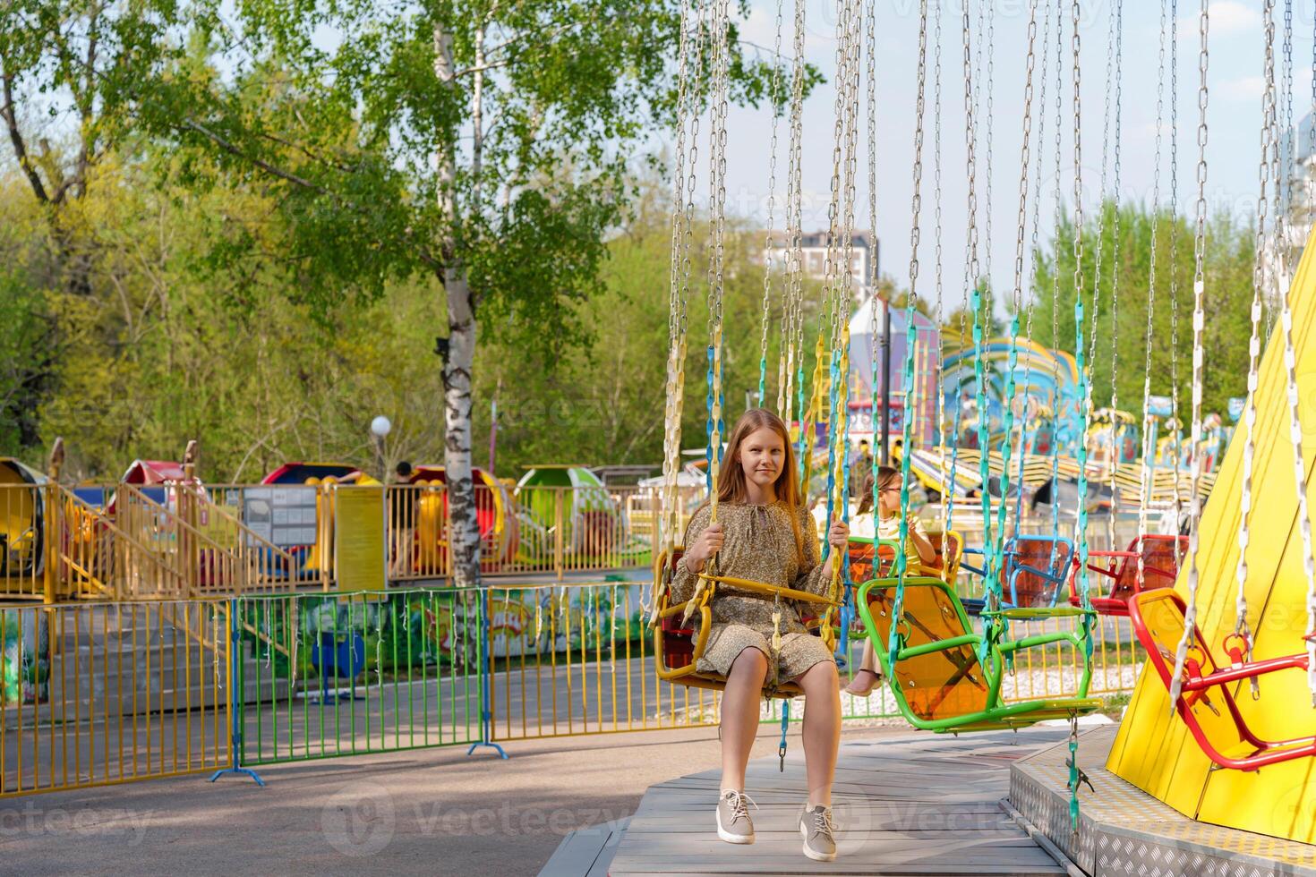 girl sits hesitantly on an amusement park swing, her expression reflecting trepidation and determination as she prepares to conquer her fears on a summer day photo
