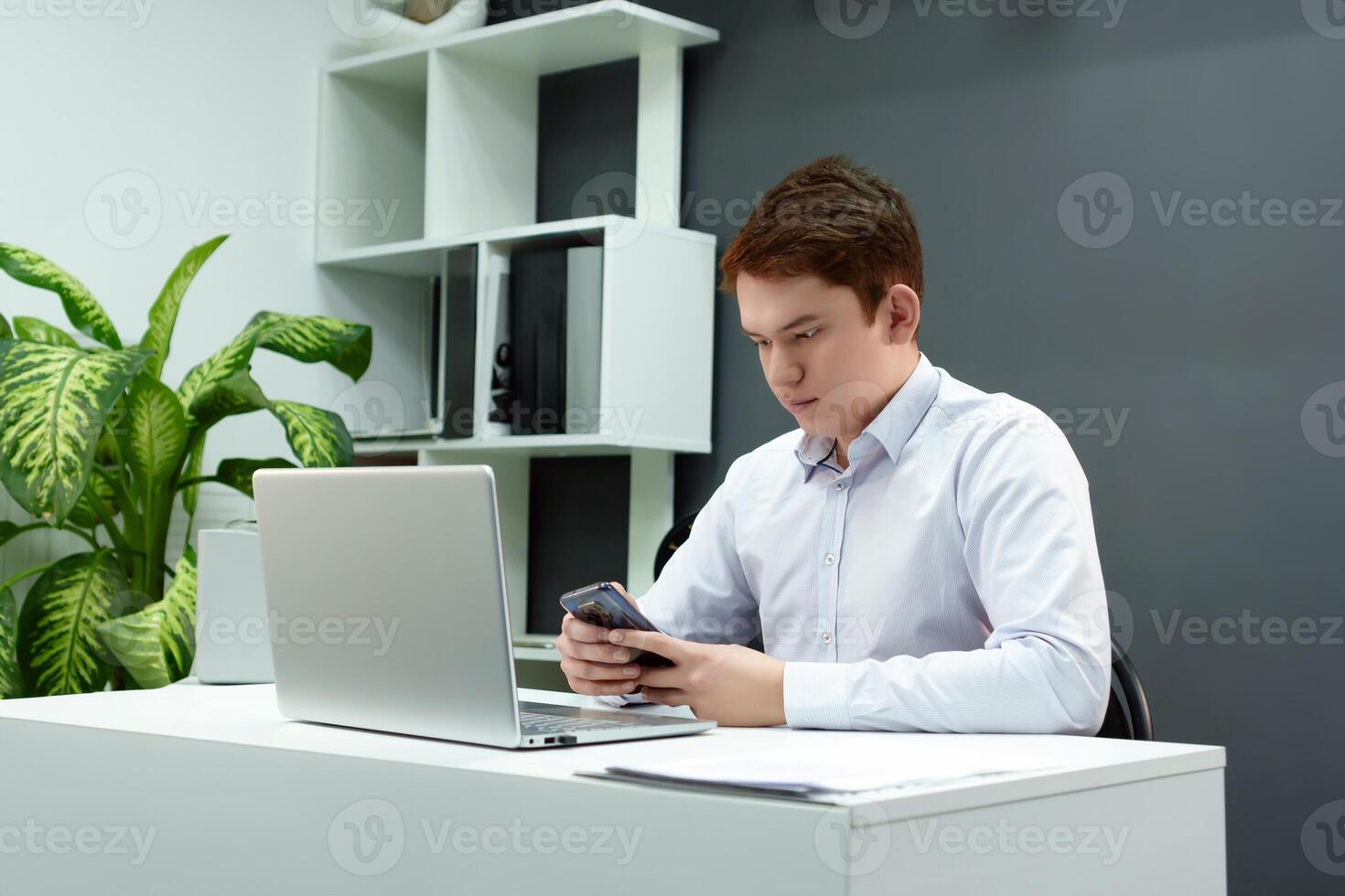 An enterprising man successfully conducts business correspondence over the phone while sitting in front of a computer monitor in a modernly decorated office space photo