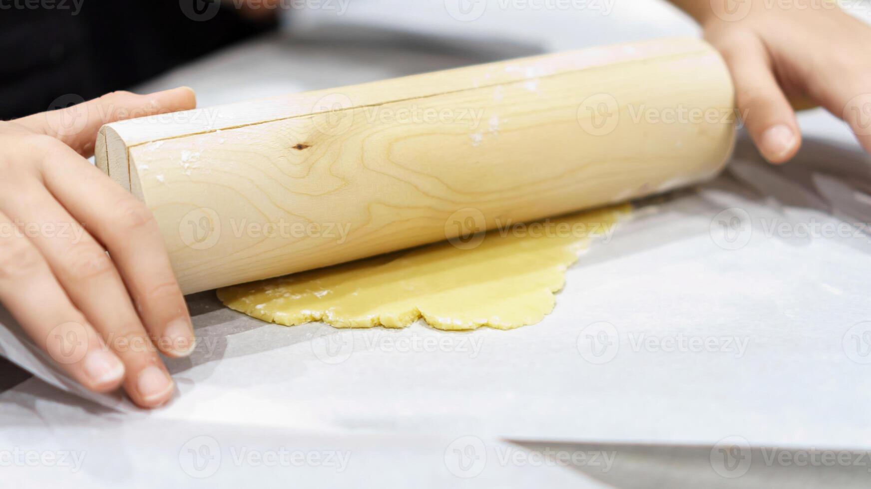 Teenage hands deftly rolling out dough with a wooden rolling pin, capturing the artisanal steps involved in crafting homemade baked goods photo
