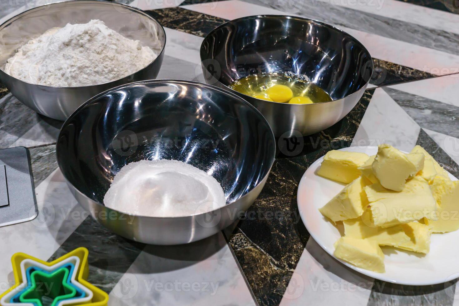 Classic baking essentials like flour, sugar, eggs, and butter presented in metal mixing containers, accompanied by festive cookie cutters, evoking the warmth of home-baked goodness photo