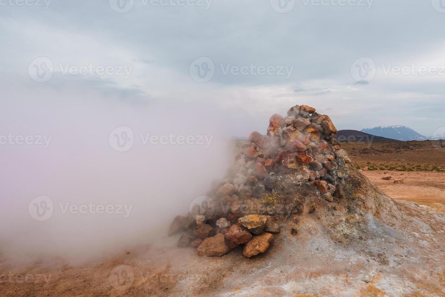 Geothermal Steam Vent with Snow-Capped Mountains in Iceland's Rugged Landscape photo