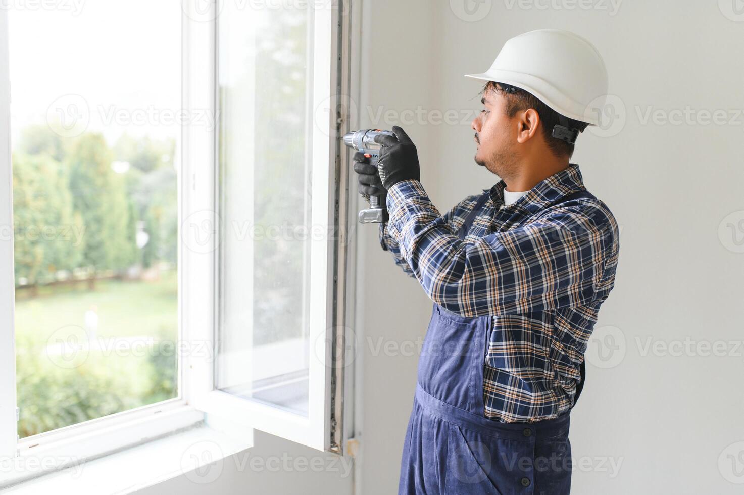 Indian Workman in overalls installing or adjusting plastic windows in the living room at home photo