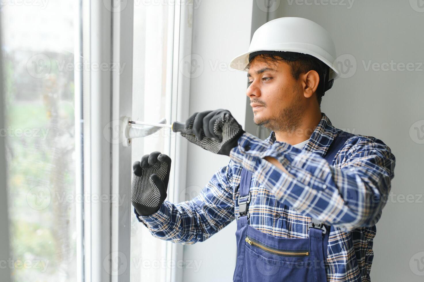 Indian Workman in overalls installing or adjusting plastic windows in the living room at home photo