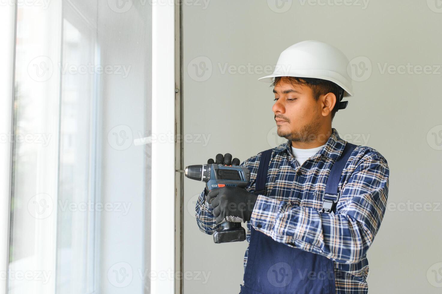 Indian Workman in overalls installing or adjusting plastic windows in the living room at home photo