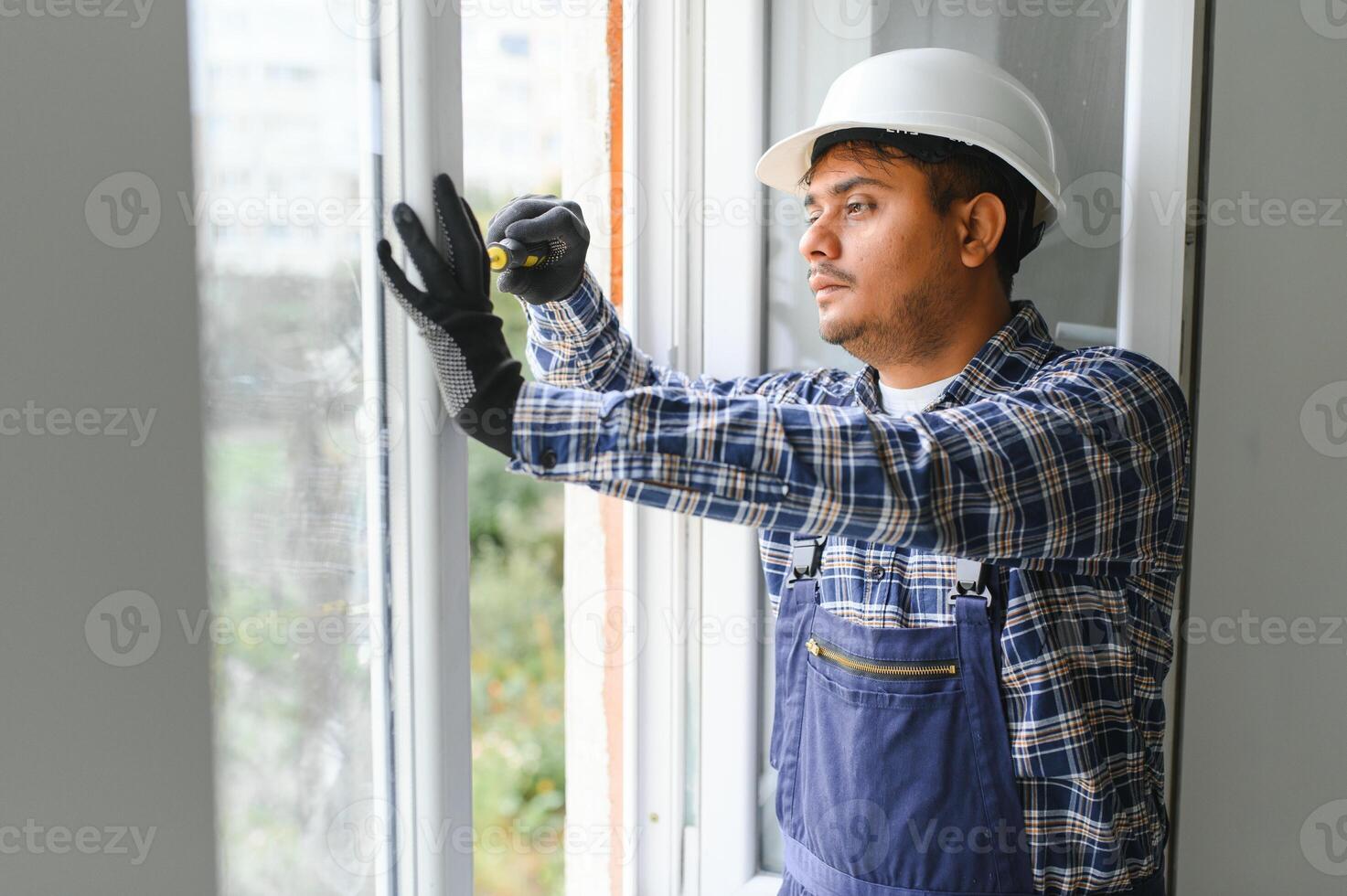 Indian Workman in overalls installing or adjusting plastic windows in the living room at home photo