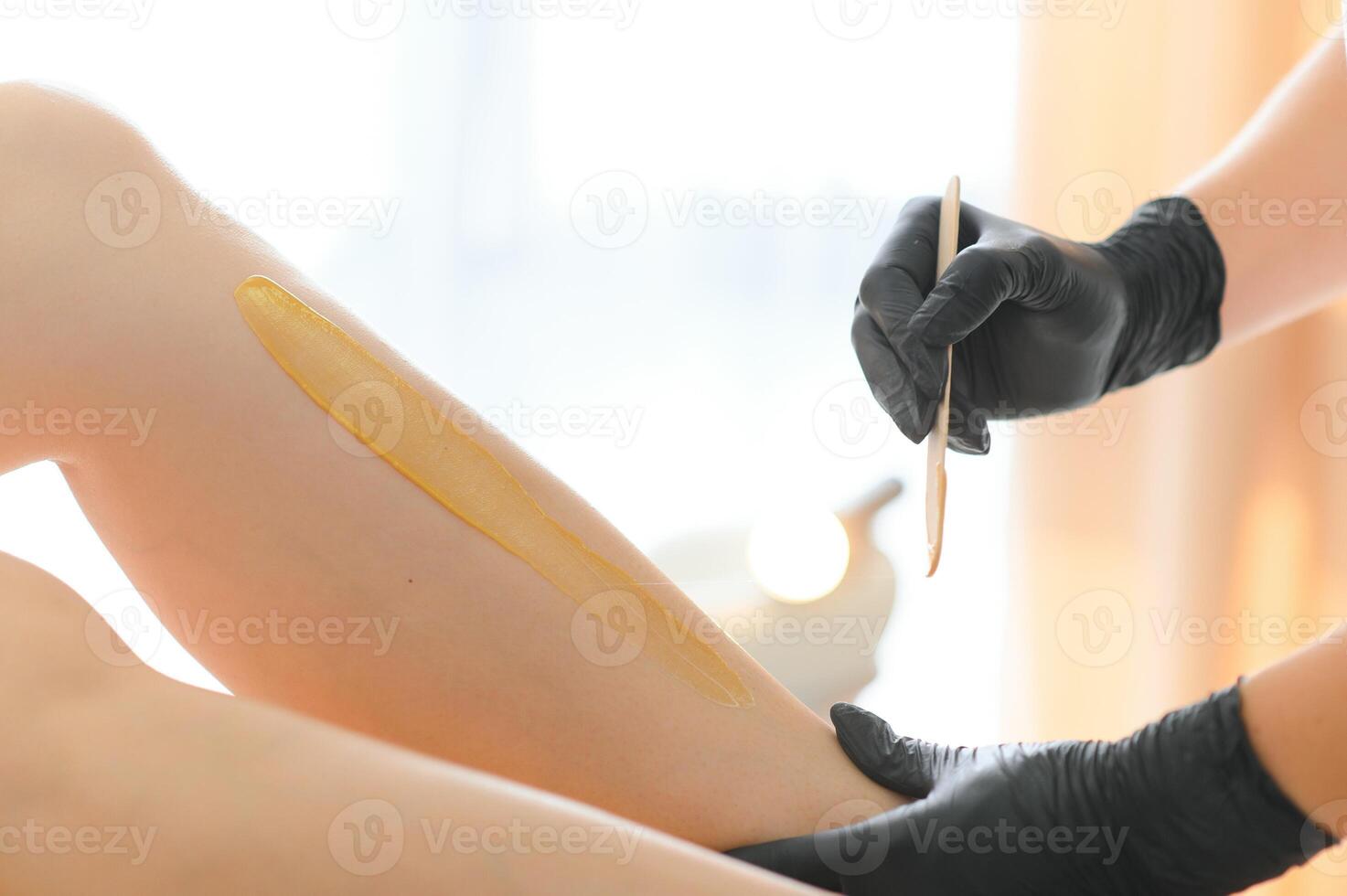 Young woman depilating legs with liquid sugar in spa center photo