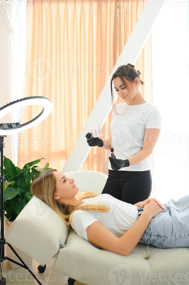 Cosmetologist applying permanent make up eyebrows for a client in a salon photo