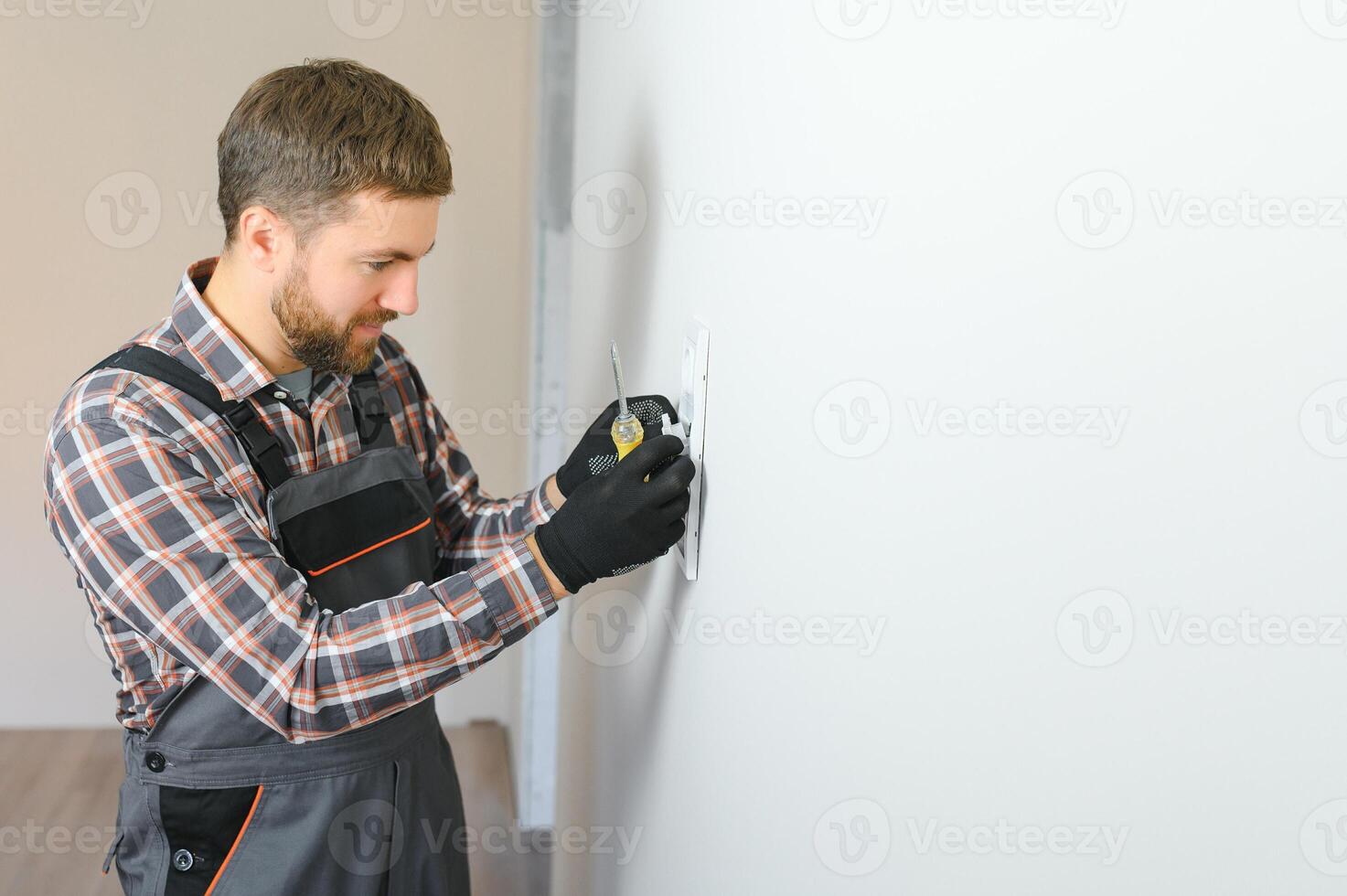 Electrician with screwdriver repairing power socket in room photo