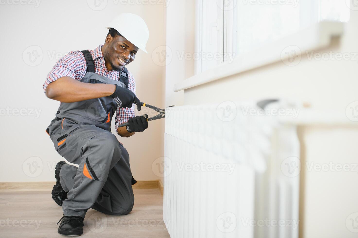 Man in workwear overalls using tools while installing or repairing heating radiator in room photo