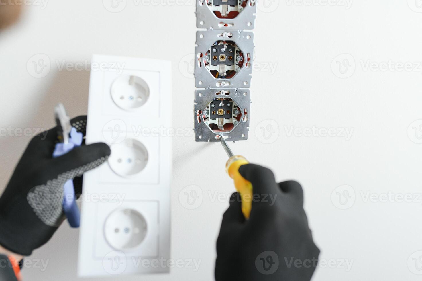 Confident professional electrician in uniform using screwdriver while replacing a socket in apartment after renovation work. photo