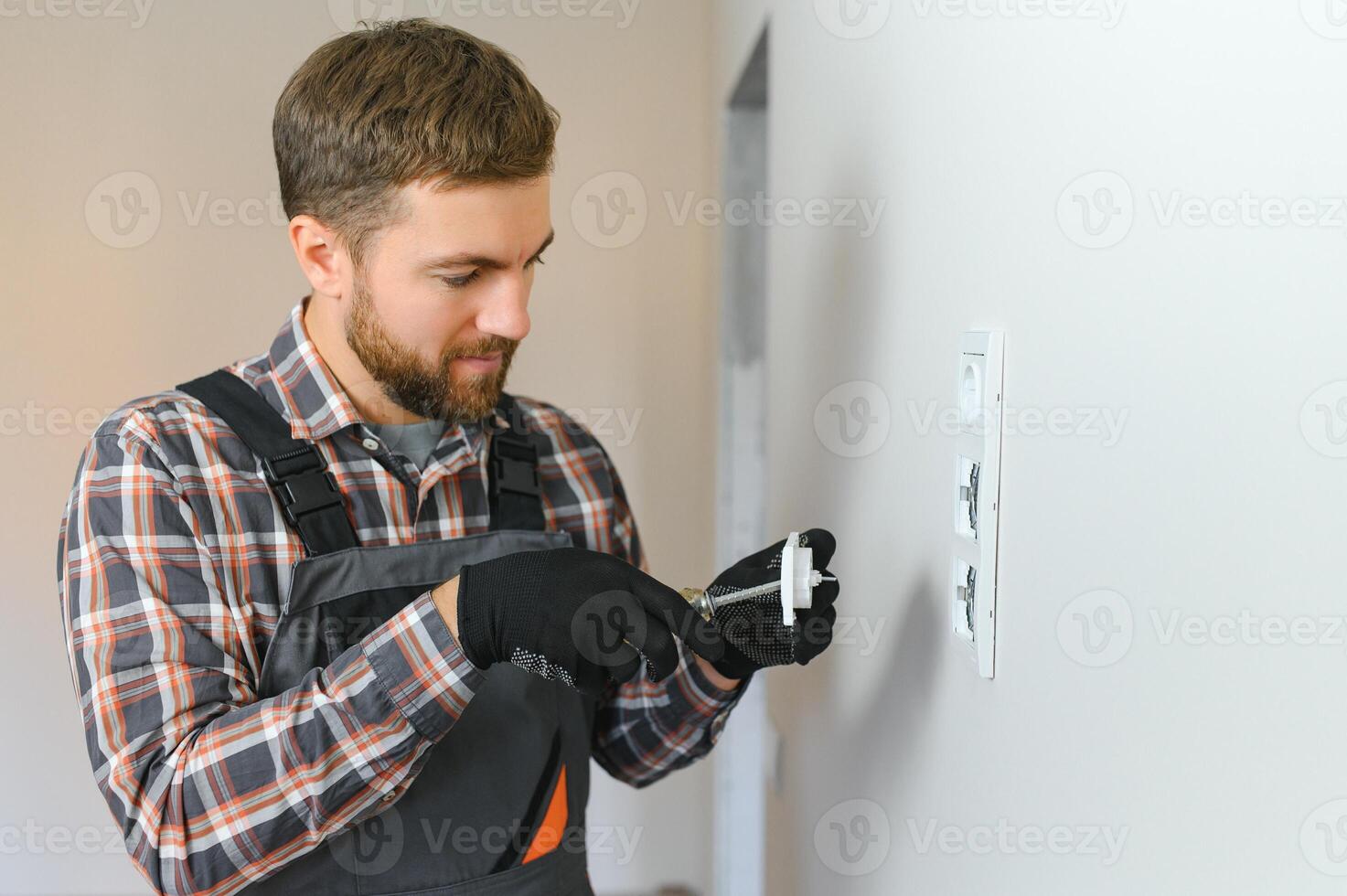 Electrician with screwdriver repairing power socket in room photo