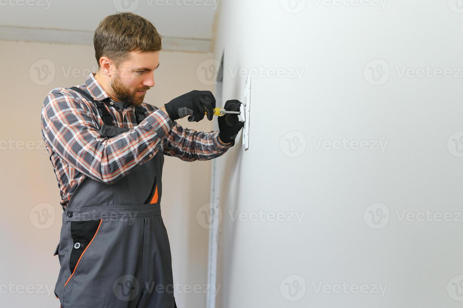 Electrician with screwdriver repairing power socket in room photo